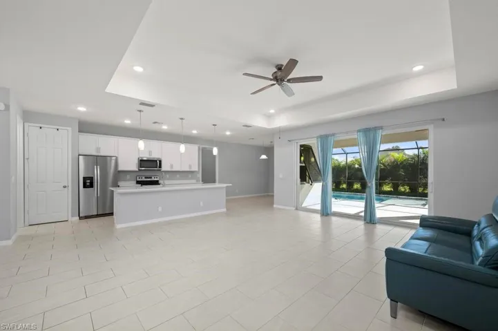 Open-concept living space featuring a tray ceiling, recessed lighting, tile flooring, kitchen with white cabinetry and a breakfast bar, and sliding glass doors leading to a screened pool area