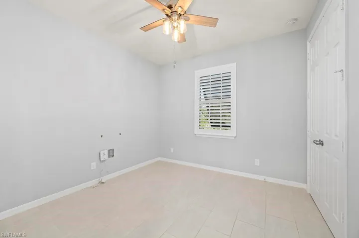 Neutral-toned room featuring large-format tile flooring, a multi-blade ceiling fan with integrated lighting, and plantation shutters