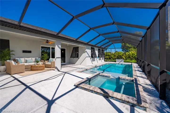 Screen-enclosed patio featuring a concrete deck, built-in swimming pool, elevated spa with stone-style edging, and a covered lanai area with a ceiling fan
