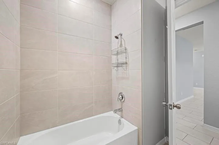 Full-height bathtub enclosure featuring neutral-toned ceramic wall tile, built-in tub, and chrome plumbing fixtures