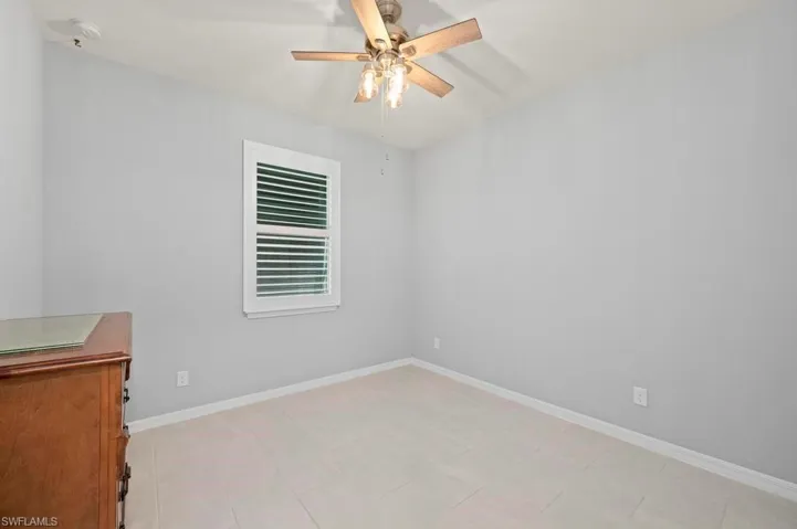 Neutral interior space featuring tile flooring, a multi-blade ceiling fan with integrated lighting, and a single-hung window with plantation shutters