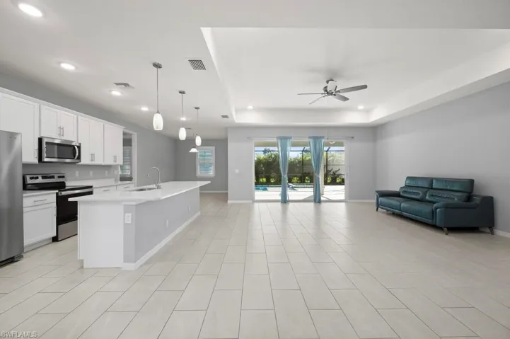 Open-concept kitchen featuring white shaker-style cabinetry, quartz countertops, a central island with a stainless steel sink, recessed lighting, and tile flooring throughout