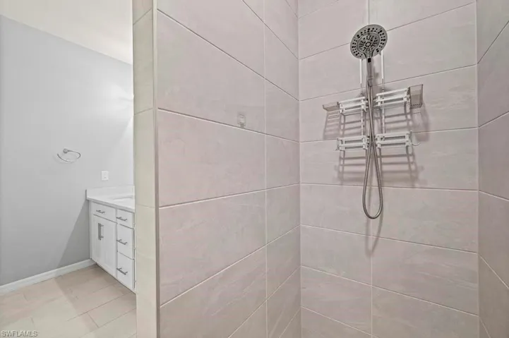 Walk-in shower featuring large-format stone-finish tile surround and adjustable multi-function shower head, paired with a white vanity cabinet and integrated solid surface countertop