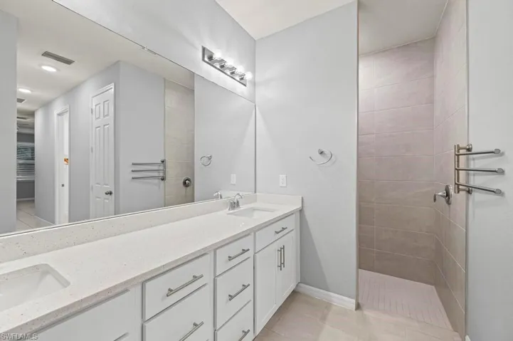 Dual-sink vanity with composite countertop, full-width wall mirror, chrome fixtures, and tiled walk-in shower