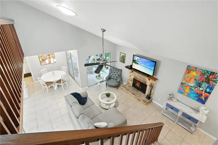 Living room featuring a fireplace, light tile patterned floors, ceiling fan, and high vaulted ceiling