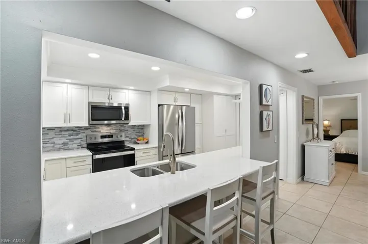 Kitchen with appliances with stainless steel finishes, tasteful backsplash, light stone countertops, light tile patterned flooring, and recessed lighting