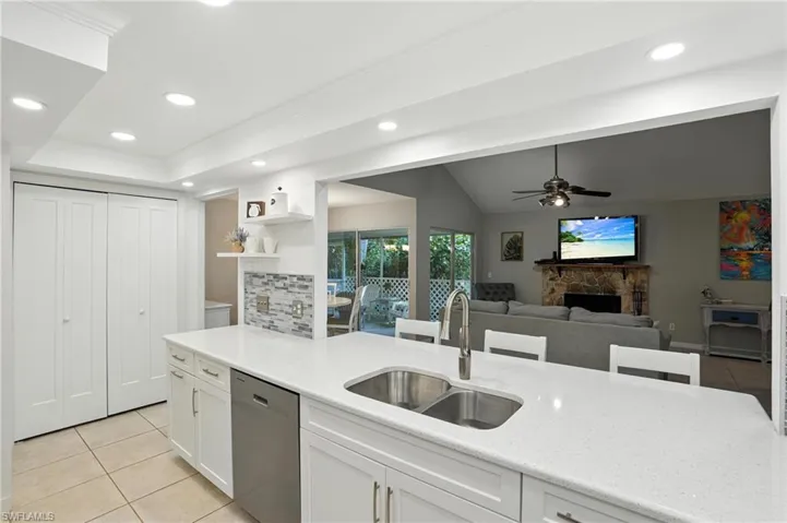 Kitchen with stainless steel dishwasher, light tile patterned floors, a fireplace, white cabinetry, and ceiling fan