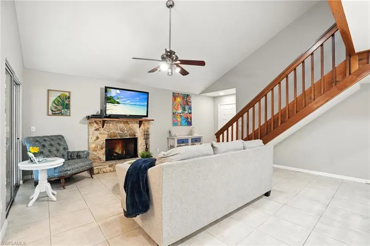 Living room featuring light tile patterned floors, stairway, a ceiling fan, a stone fireplace, and high vaulted ceiling