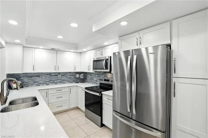 Kitchen featuring appliances with stainless steel finishes, ornamental molding, tasteful backsplash, recessed lighting, and white cabinetry
