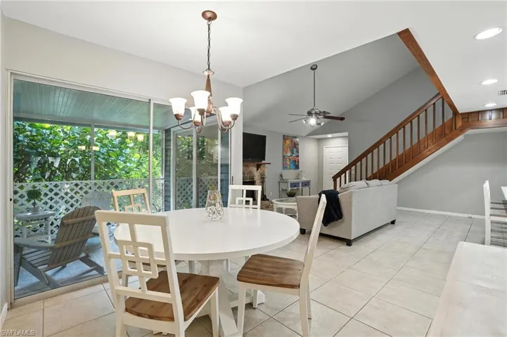 Dining room featuring a ceiling fan, light tile patterned floors, stairs, a chandelier, and vaulted ceiling