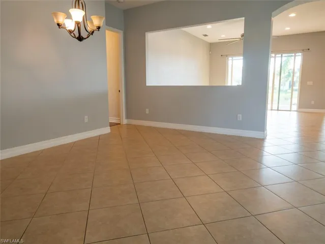 Unfurnished room featuring light tile patterned floors, a ceiling fan, arched walkways, and a chandelier