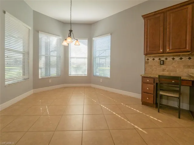 Unfurnished dining area featuring light tile patterned floors, built in desk, and a chandelier