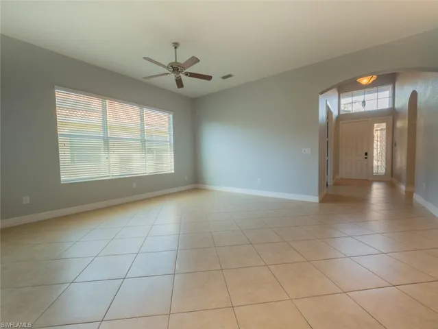 Unfurnished room with arched walkways, a ceiling fan, and light tile patterned floors