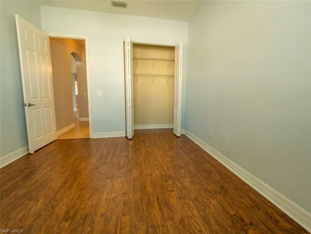 Unfurnished bedroom featuring arched walkways, a closet, and wood finished floors