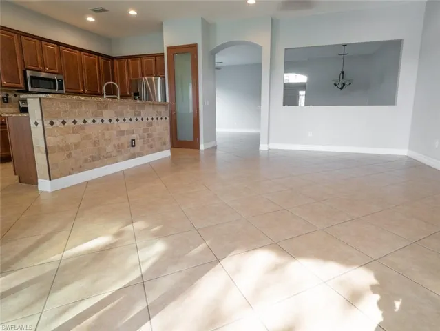 Kitchen featuring arched walkways, stainless steel appliances, an island with sink, and light tile patterned floors