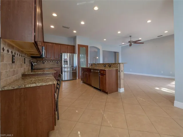 Kitchen featuring light stone countertops, stainless steel appliances, light tile patterned floors, a kitchen island with sink, and recessed lighting