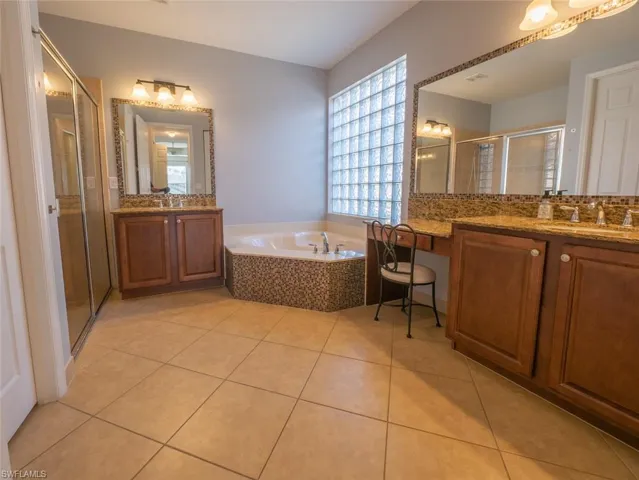 Bathroom featuring two vanities, a stall shower, light tile patterned floors, and a bath