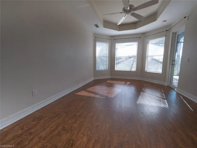 Unfurnished room with a tray ceiling, a ceiling fan, and dark wood-type flooring