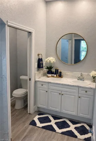 Bathroom with a textured wall, double vanity, and light wood-style floors