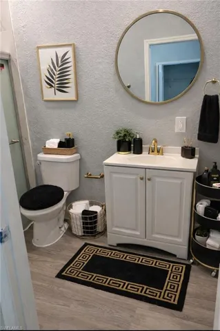 Full bath with vanity, light wood finished floors, a textured wall, and a shower with door