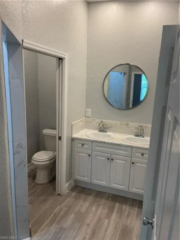 Full bath with a textured wall, light wood-style floors, and double vanity