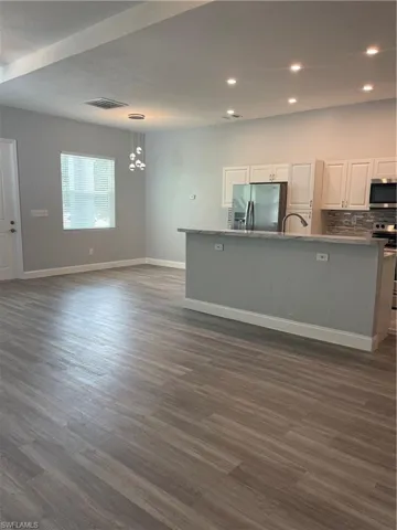 Kitchen featuring white cabinets, open floor plan, dark wood-style flooring, tasteful backsplash, and fridge