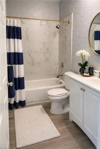 Bathroom with a textured wall, vanity, light wood-style floors, and shower / tub combo