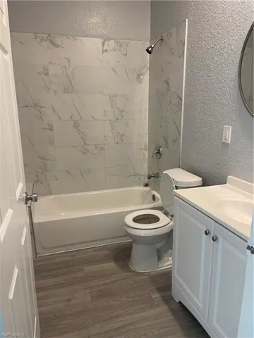 Bathroom featuring a textured wall, shower / tub combination, vanity, and dark wood-style floors