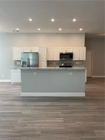 Kitchen featuring white cabinetry, backsplash, fridge, recessed lighting, and an island with sink