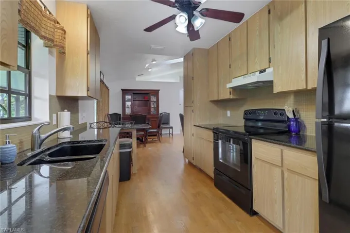 Kitchen featuring sink, black appliances, light wood-type flooring, and tasteful backsplash