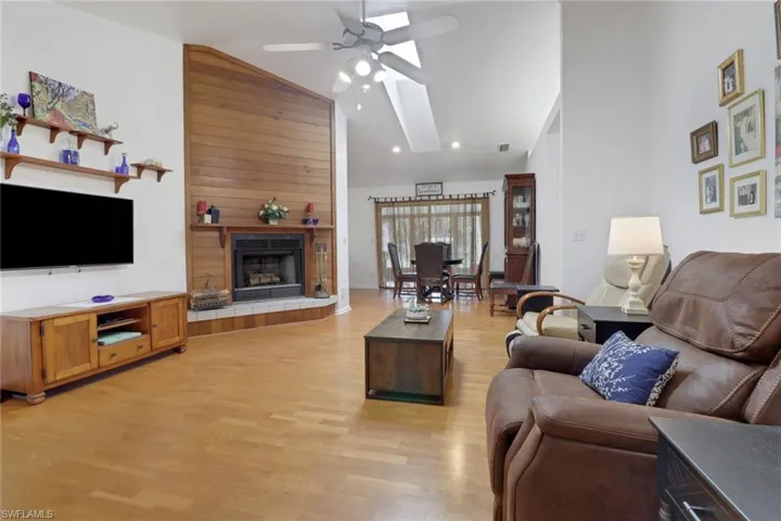 Living room with wood walls, light hardwood / wood-style flooring, a tiled fireplace, high vaulted ceiling, and ceiling fan