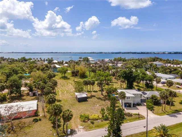 Expansive property featuring a contemporary residence, mature palm trees, a concrete driveway, and direct street access, with distant water visible