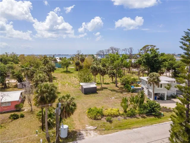Expansive property featuring a two-story residence, mature palm trees, various shrubbery, a detached shed, and distant water