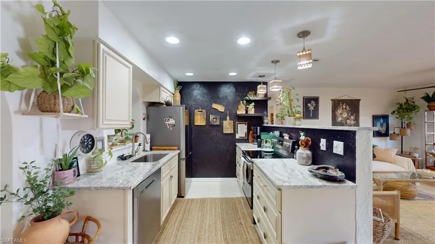 Kitchen with stainless steel appliances, sink, pendant lighting, and light stone counters