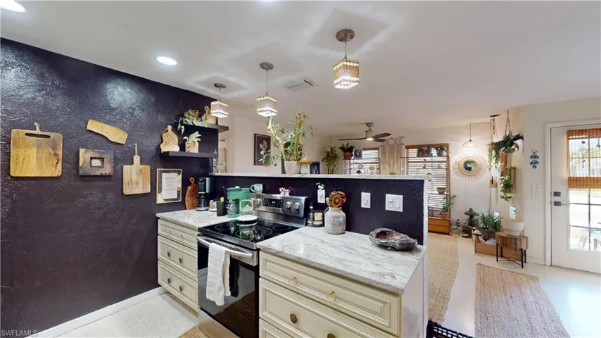 Kitchen with stainless steel electric range oven, decorative light fixtures, ceiling fan, light stone countertops, and cream cabinetry