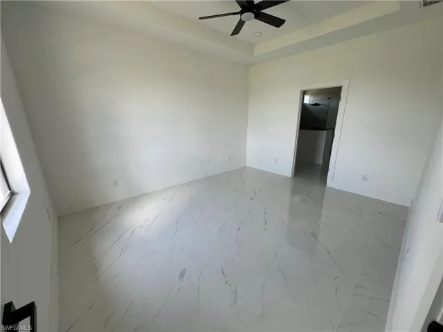 Empty room featuring a tray ceiling, ceiling fan, and light tile patterned flooring