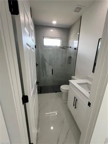 Bathroom with a shower with door, toilet, tile patterned floors, and vanity