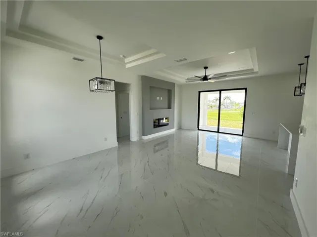 Unfurnished living room featuring ceiling fan, a raised ceiling, and light tile patterned floors