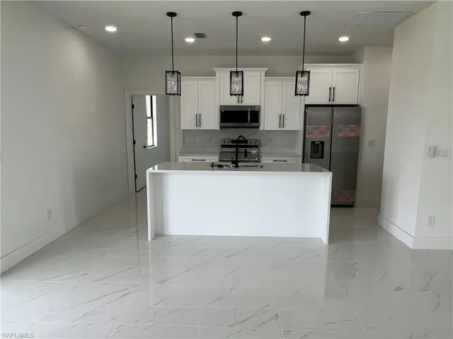 Kitchen with a kitchen island with sink, white cabinets, light tile patterned floors, and stainless steel appliances