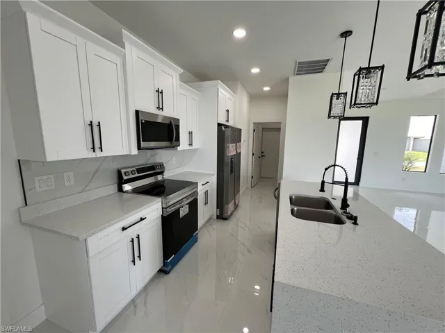 Kitchen with appliances with stainless steel finishes, decorative backsplash, sink, light stone counters, and white cabinets