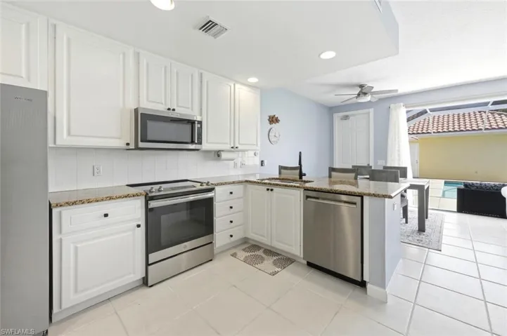 Kitchen with stainless steel appliances, light stone counters, white cabinets, a peninsula, and recessed lighting