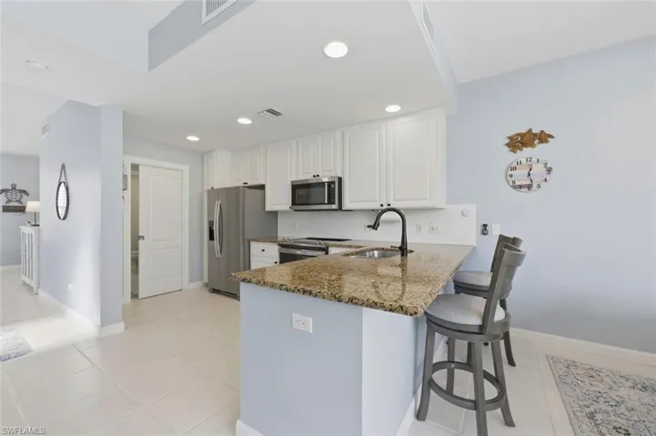 Kitchen featuring dark stone countertops, a peninsula, stainless steel appliances, a kitchen bar, and white cabinets