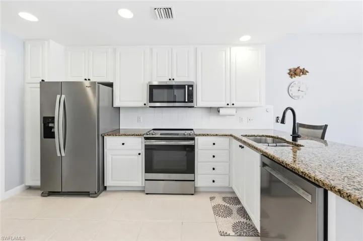 Kitchen with stainless steel appliances, dark stone countertops, white cabinets, recessed lighting, and light tile patterned floors