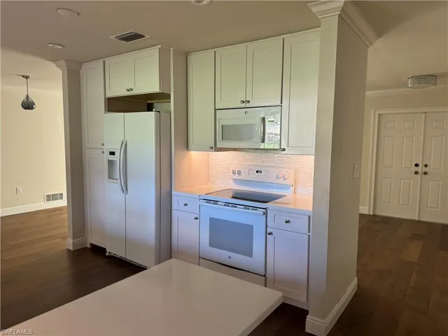 Kitchen with dark hardwood / wood-style floors, backsplash, hanging light fixtures, white appliances, and white cabinets