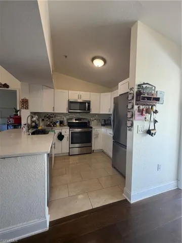 Kitchen with a textured wall, stainless steel appliances, white cabinets, light stone counters, and lofted ceiling