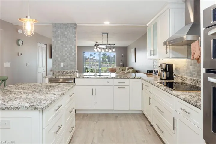Kitchen featuring decorative light fixtures, stainless steel appliances, kitchen peninsula, white cabinets, and wall chimney range hood