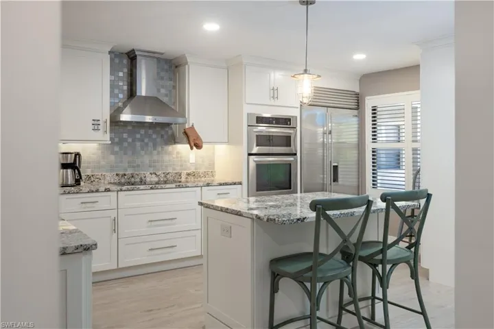 Kitchen featuring decorative light fixtures, wall chimney exhaust hood, stainless steel appliances, white cabinetry, and light wood-type flooring