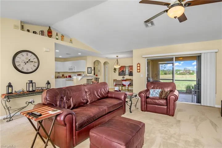 Living room featuring arched walkways, ceiling fan, lofted ceiling, light colored carpet, and visible vents