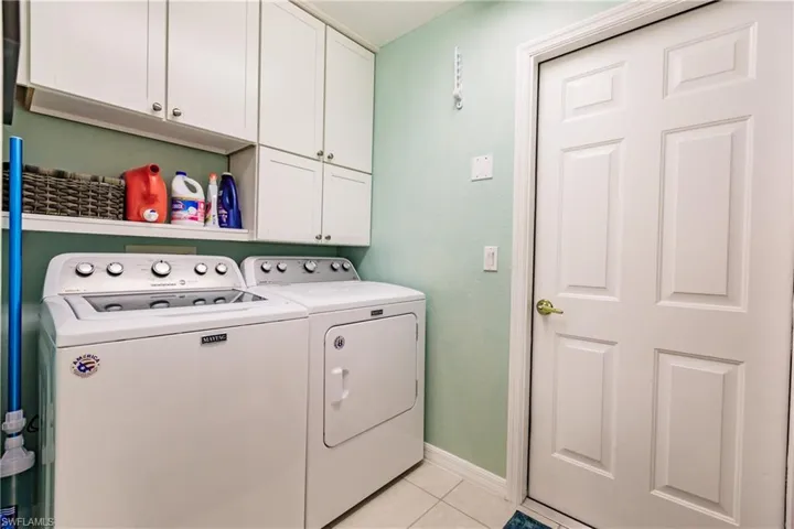 Laundry area featuring independent washer and dryer, light tile flooring, and cabinets