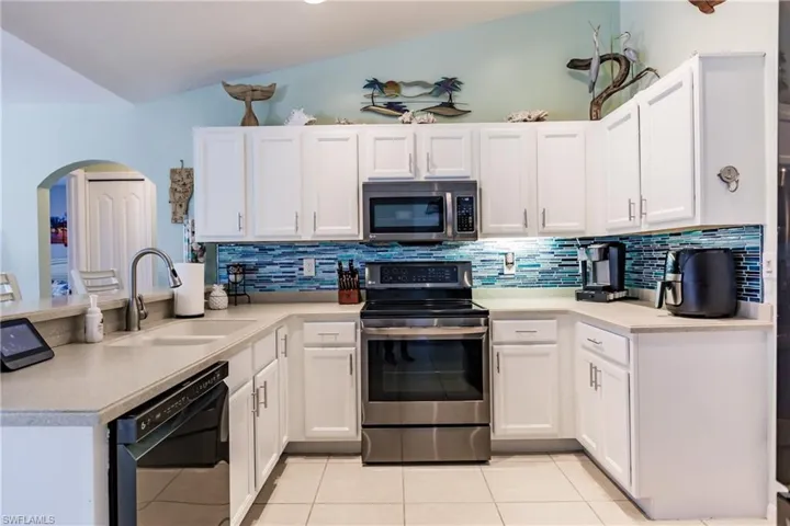 Kitchen featuring vaulted ceiling, tasteful backsplash, appliances with stainless steel finishes, sink, and light tile floors